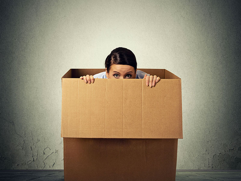 Femme qui a peur et qui se cache dans une boîte de carton.