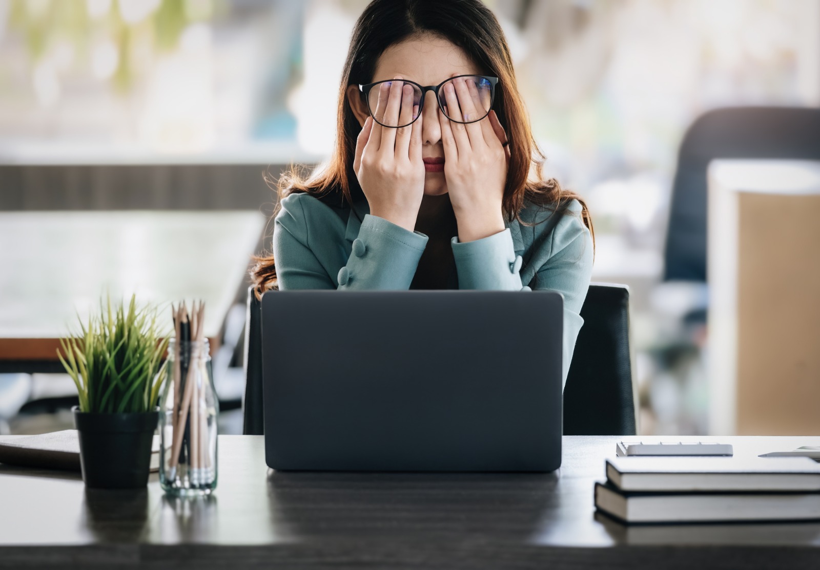 Une femme devant sa table de travail où se trouve son ordinateur. Elle se frotte les yeux, fatiguée