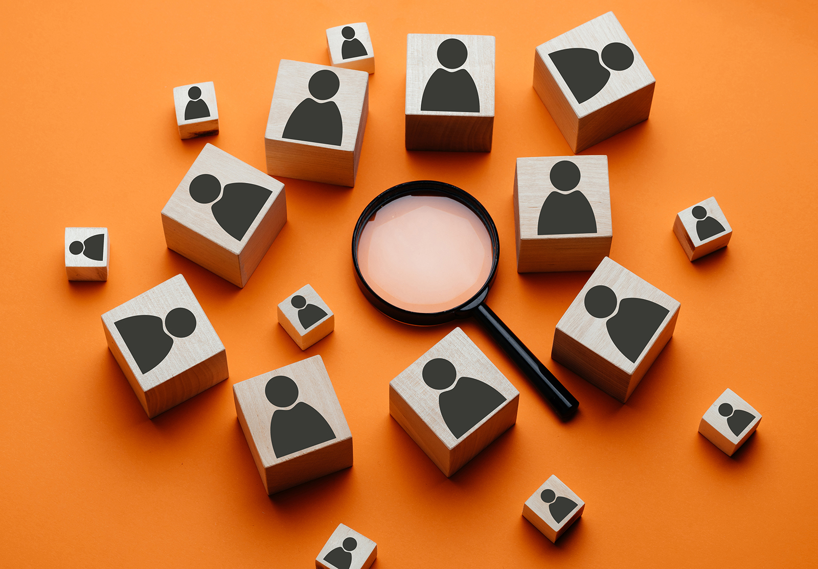 Des cubes en bois avec l'image d'un homme sont posés à côté d'une loupe sur un fond orange. Le concept de recherche de talents ou d'employés à l'aide d'une loupe. Photo de haute qualité