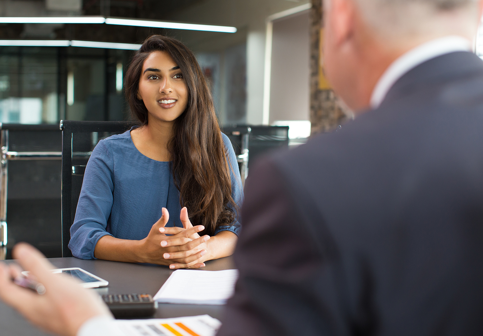 Portrait d'une jeune femme indienne, cliente ou candidate, assise à une table, discutant avec un cadre supérieur masculin et souriant dans un bureau. Entretien d'embauche ou concept de conseil