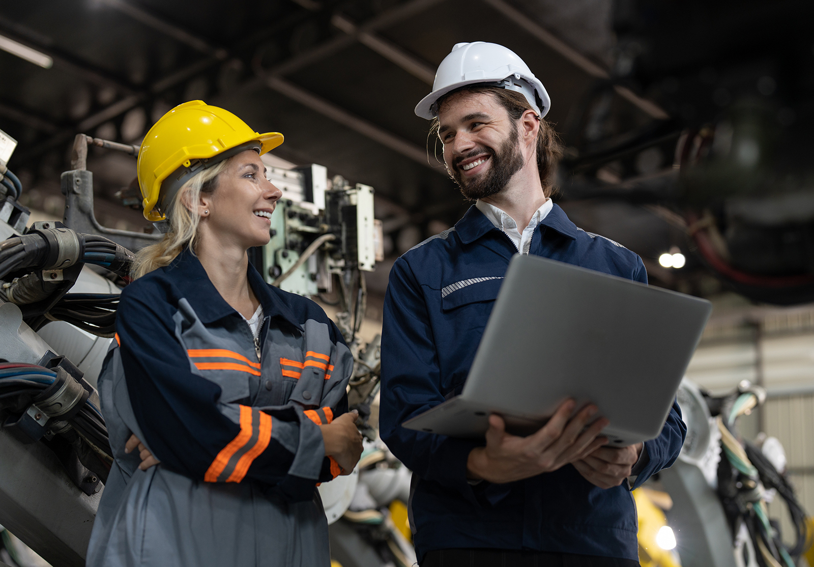 Des hommes et des femmes ingénieurs heureux avec un ordinateur portable vérifient et entretiennent le bras robotisé d'une machine à souder dans une usine d'assemblage robotisé.