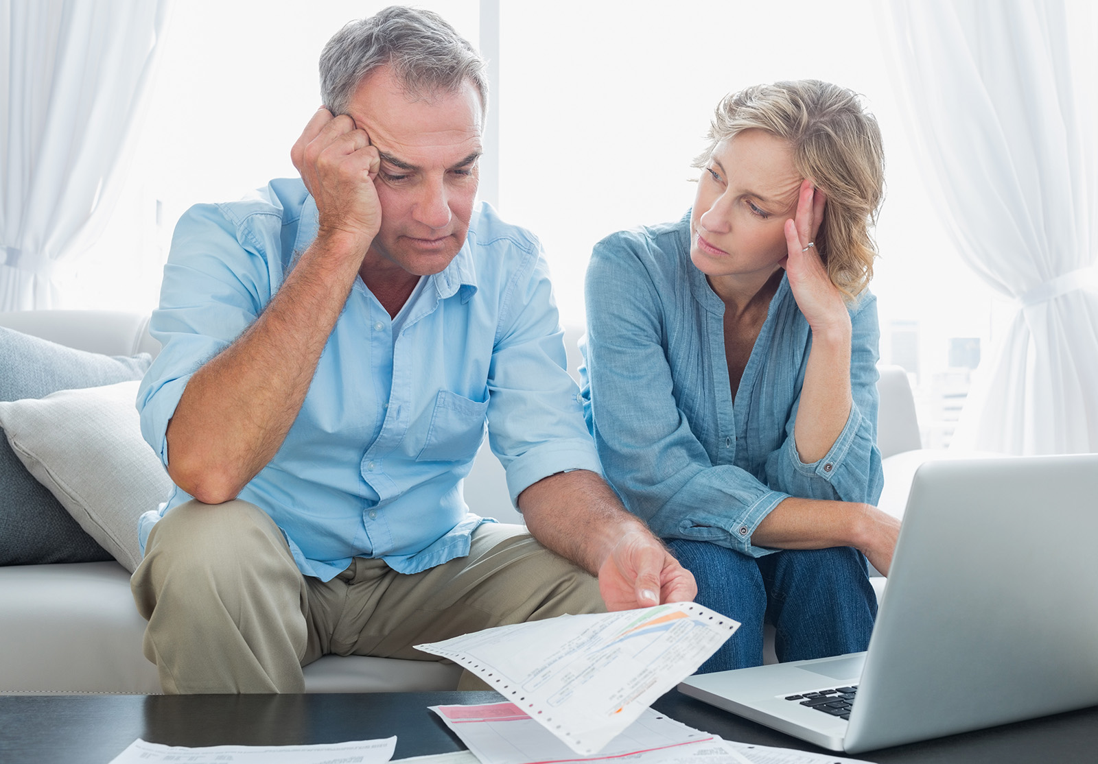 Couple inquiet utilisant son ordinateur portable pour payer ses factures à la maison, dans le salon