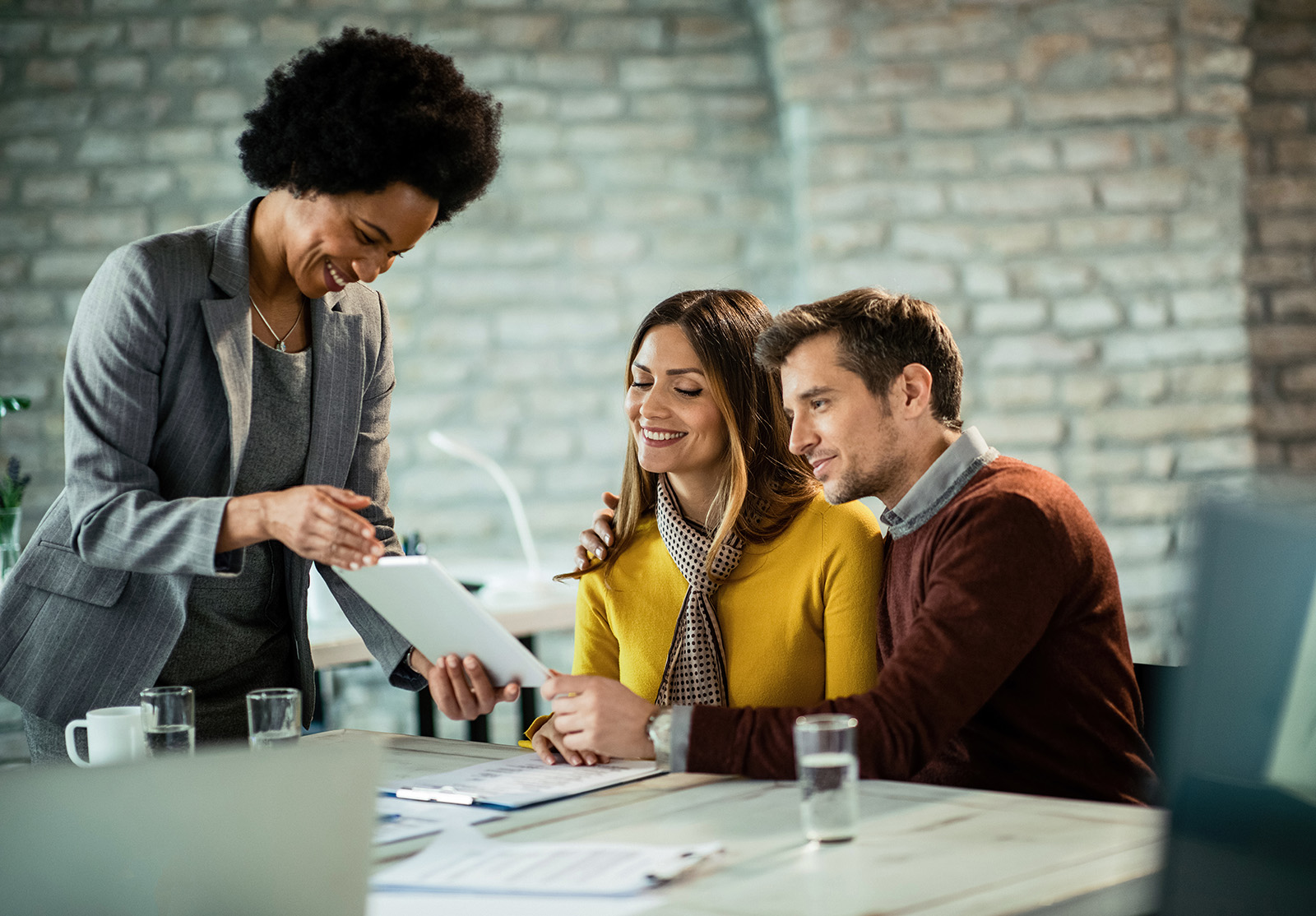 Un couple heureux et un agent d'assurance afro-américain consultent un plan d'épargne sur une tablette tactile au bureau.