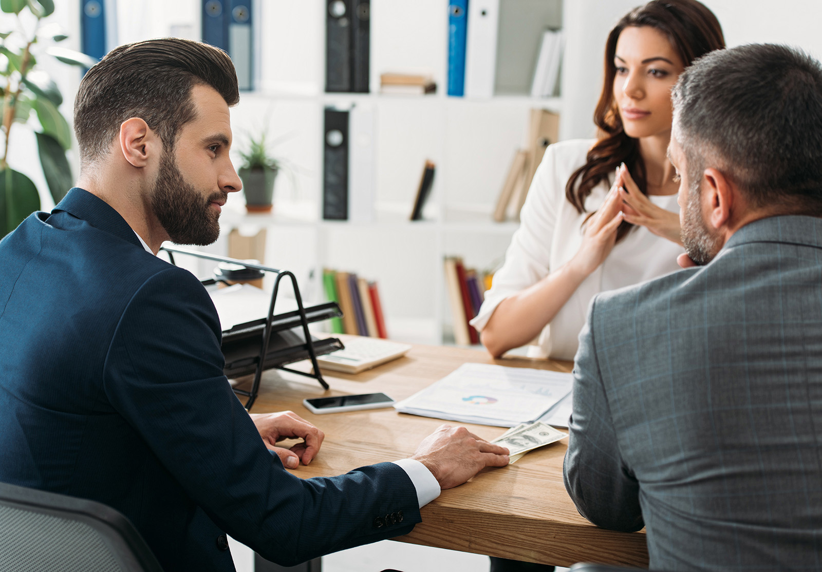 focus sélectif sur de beaux investisseurs en costume s'entretenant avec un conseiller séduisant sur leur lieu de travail