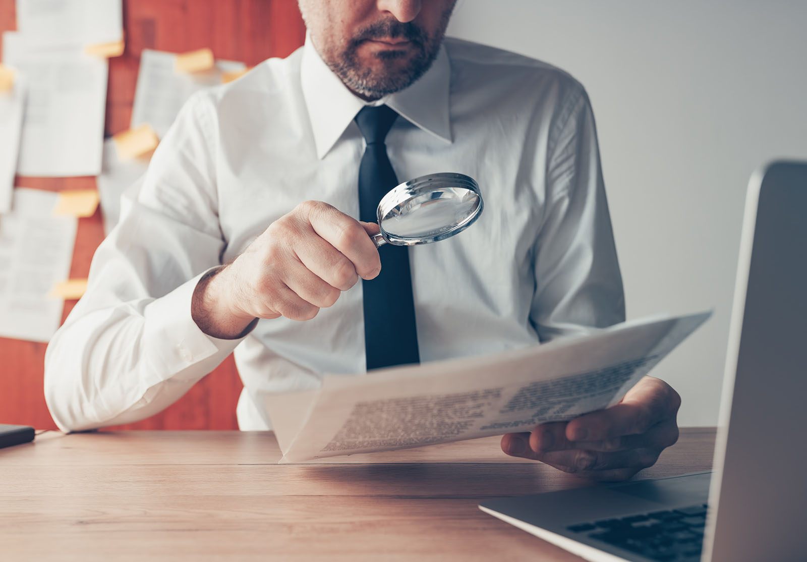 Homme d'affaires lisant des documents à la loupe sur un bureau, gros plan avec mise au point sélective.